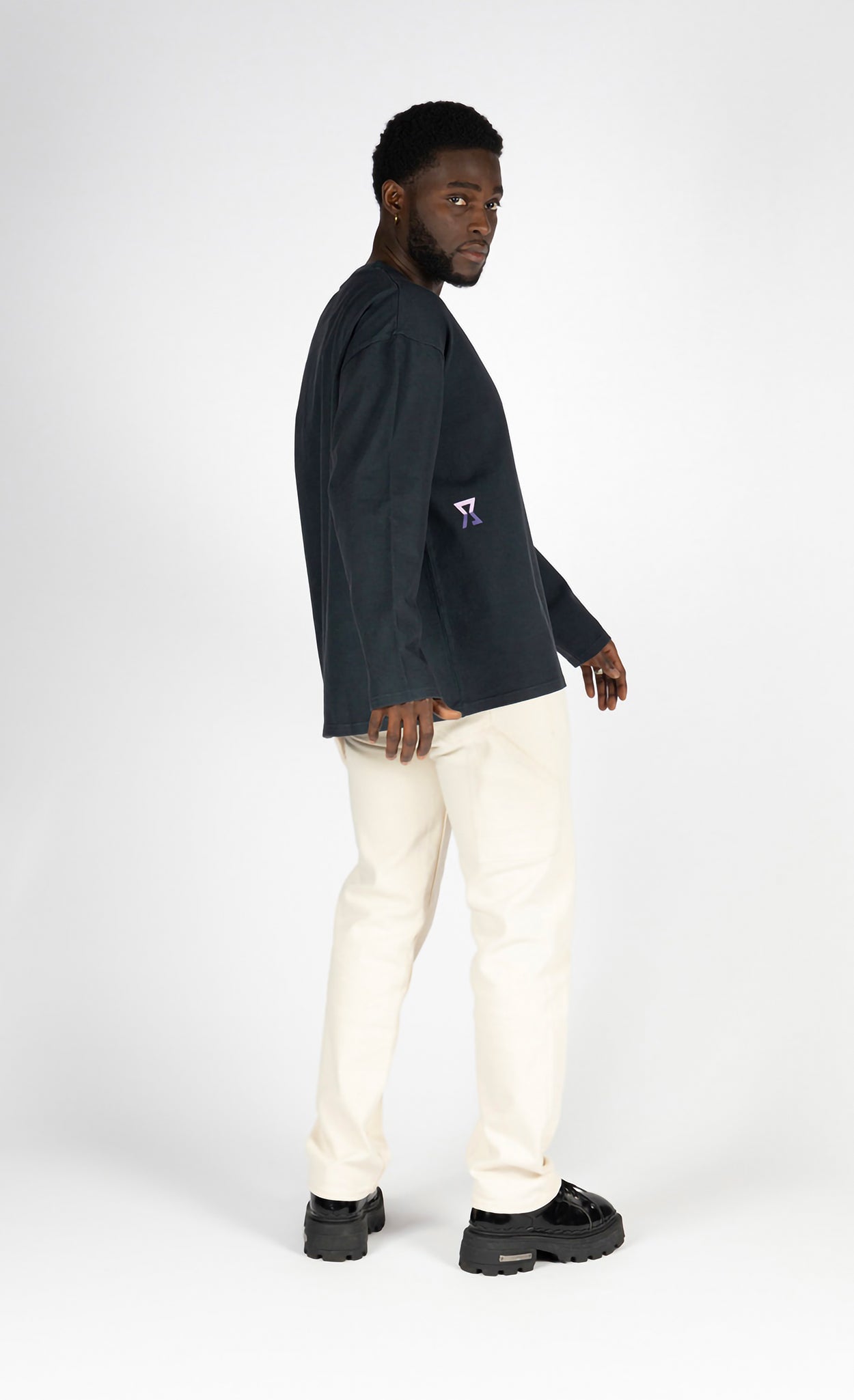 Man wearing a black long-sleeve shirt with a logo and white pants on a white background made with recycled cotton
