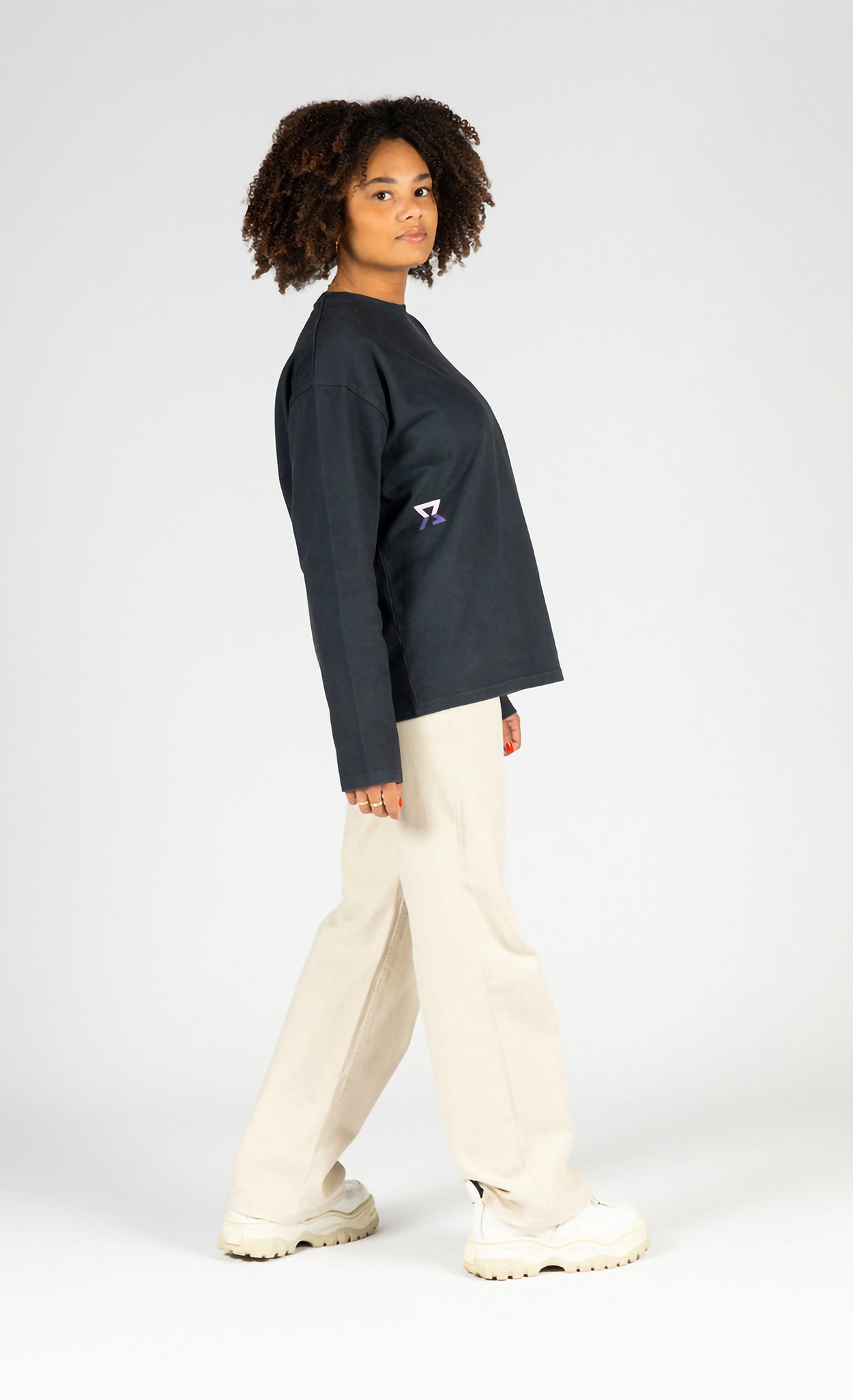 Person wearing a black sweater with a logo and white pants on a white background