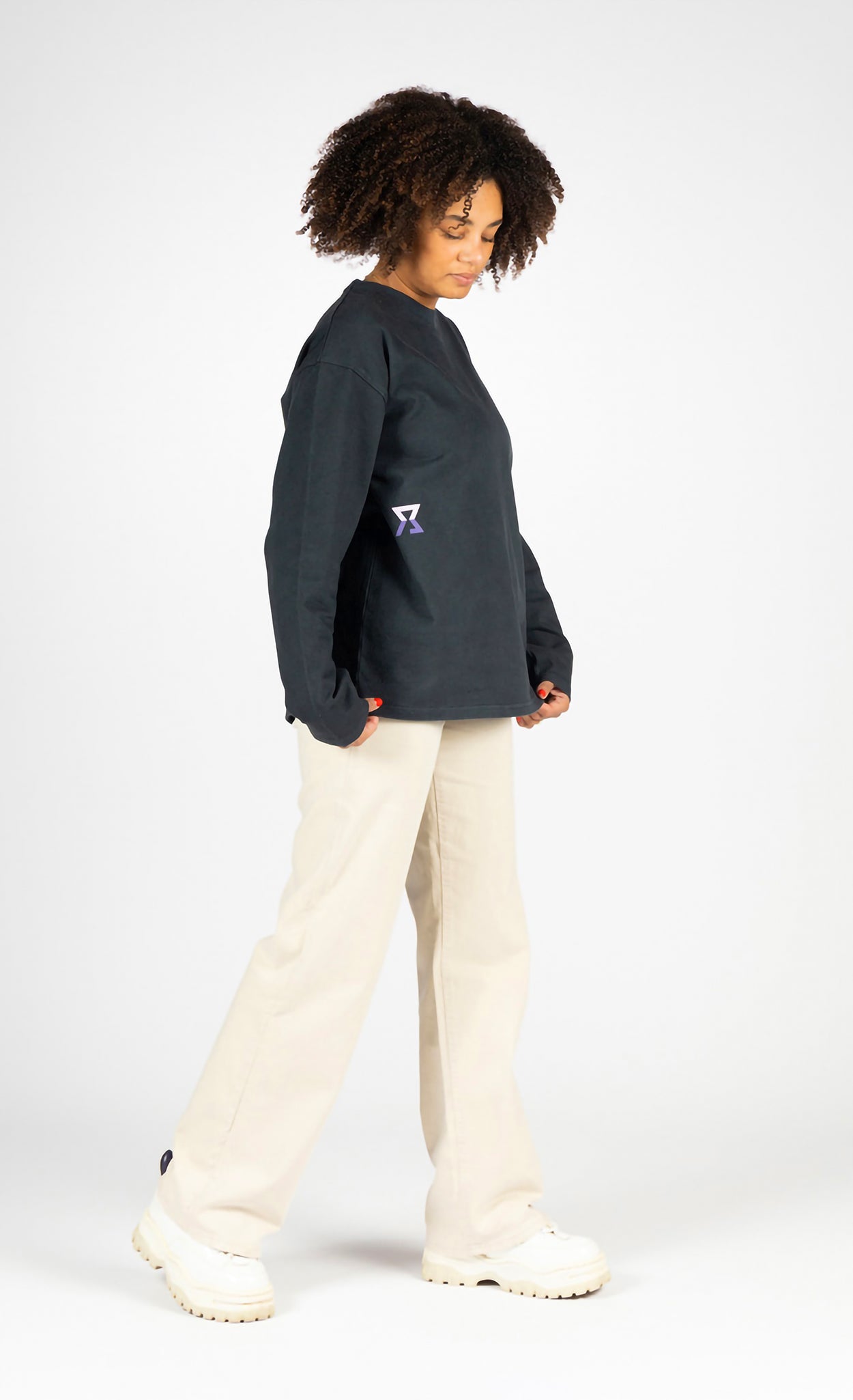 Person wearing a dark blue sweatshirt with a logo and light-colored pants on a white background
