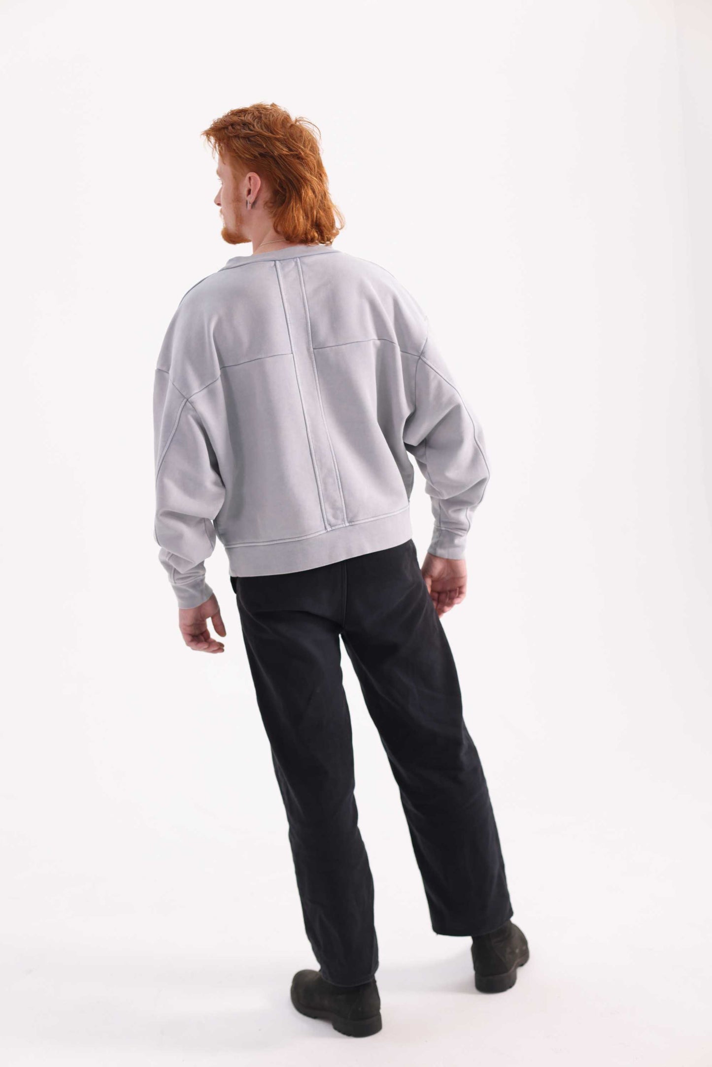 Person wearing a light gray sweatshirt and black pants on a white background