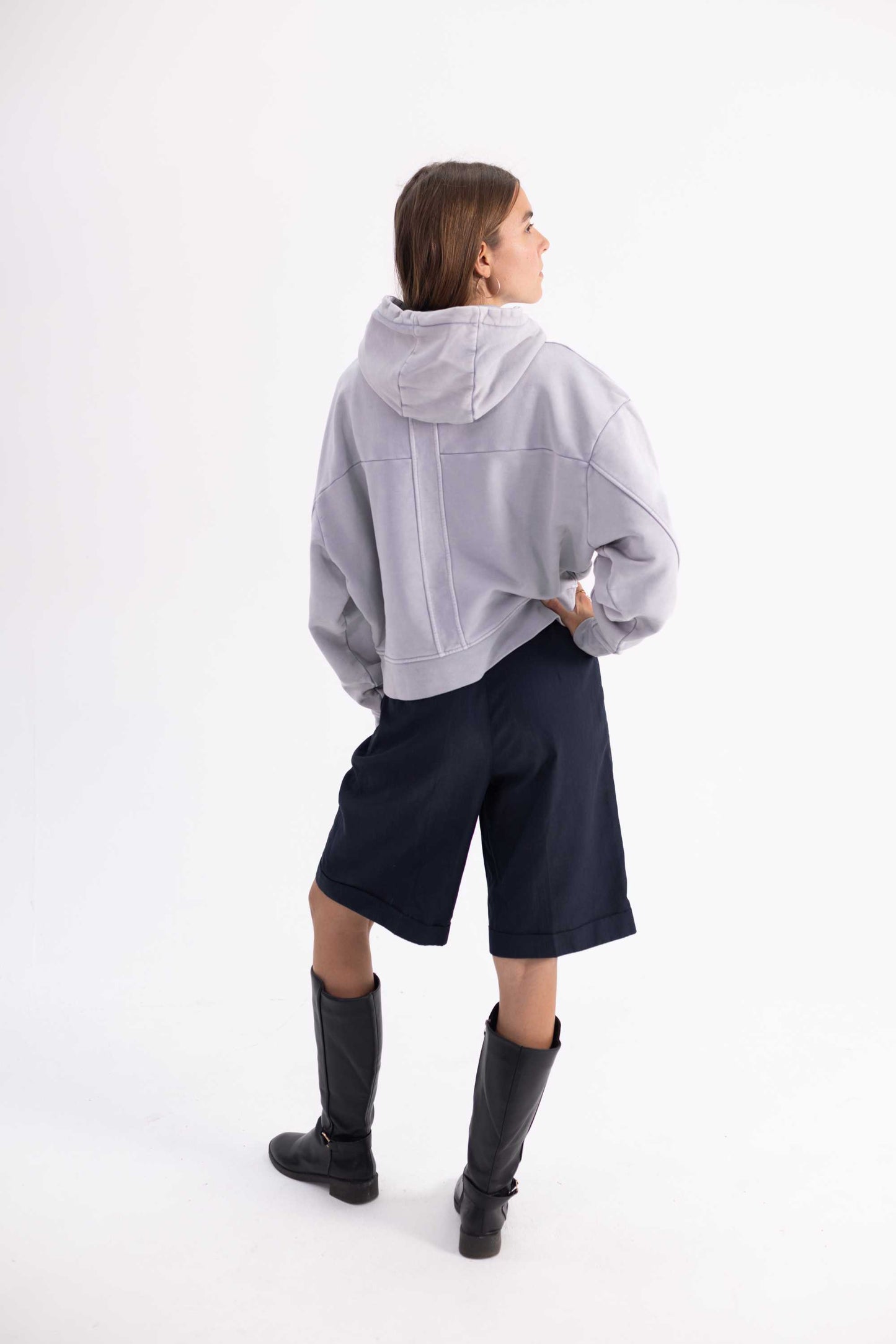 Person wearing a gray hoodie, navy shorts, and black boots on a white background