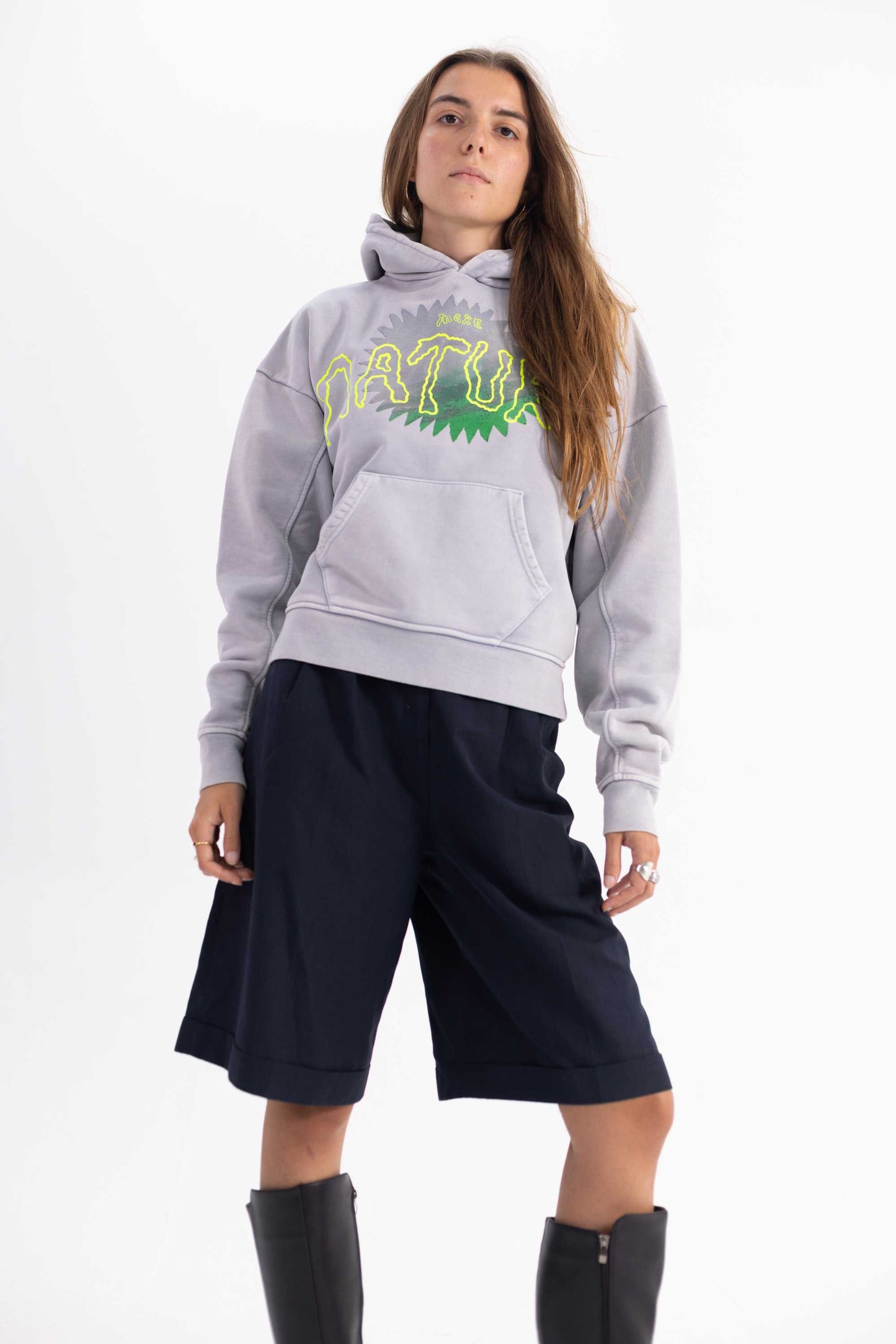 Female model wearing a ethically dyed grey hoodie with a nature logo and dark shorts on a white background