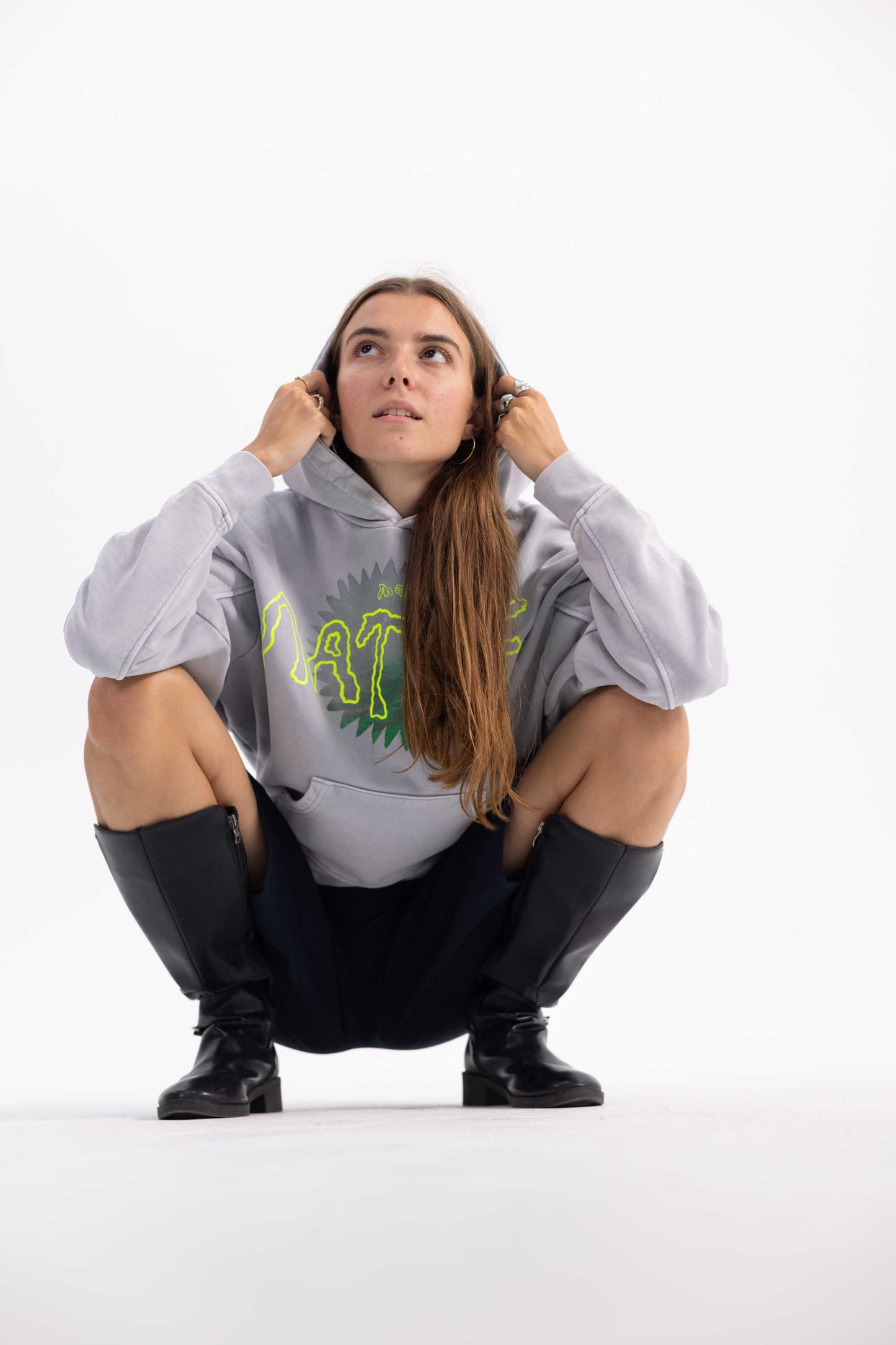 Female model wearing a gray hoodie with a nature logo and black boots on a white background