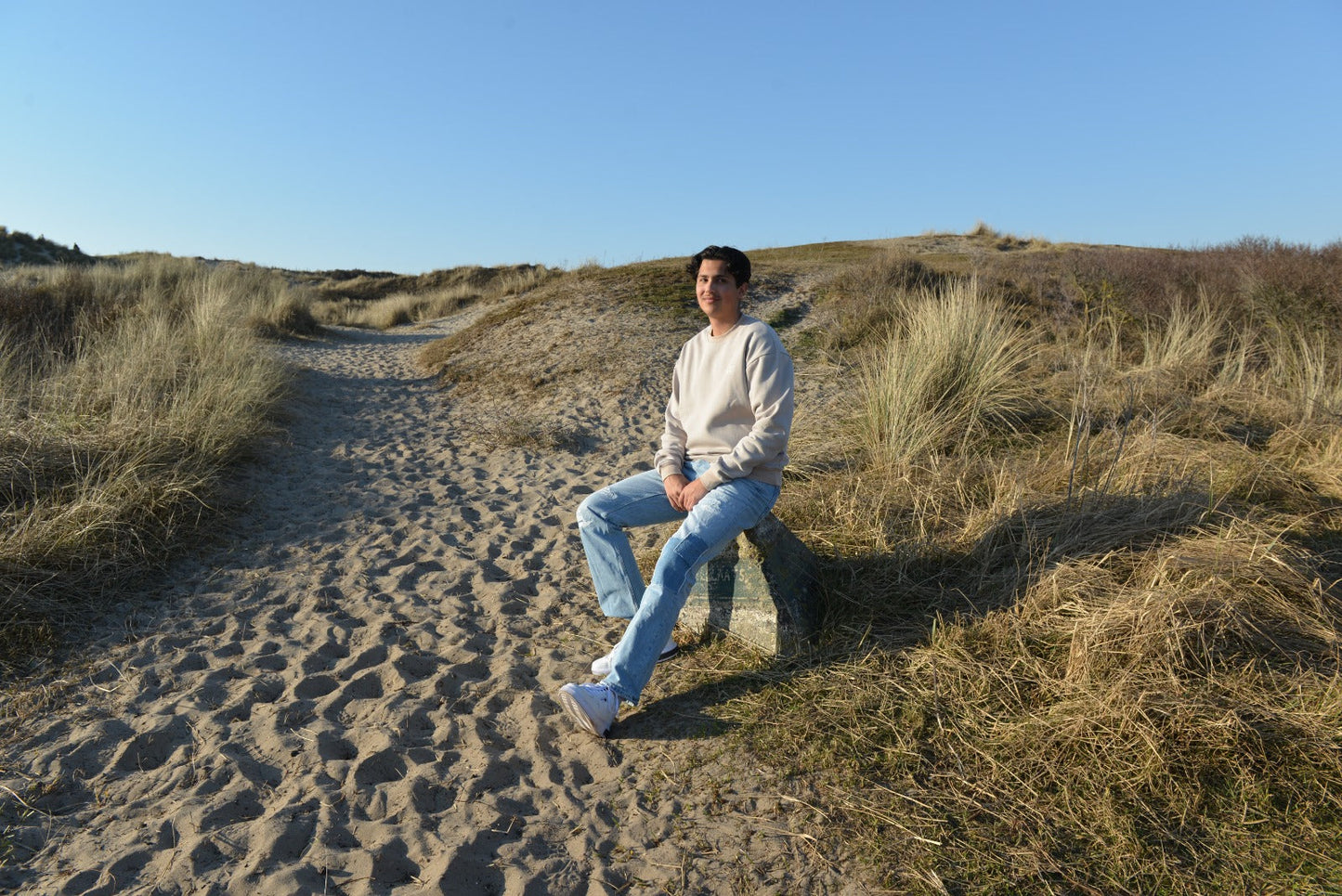 Person sitting on a sandy path in a grassy dune landscape