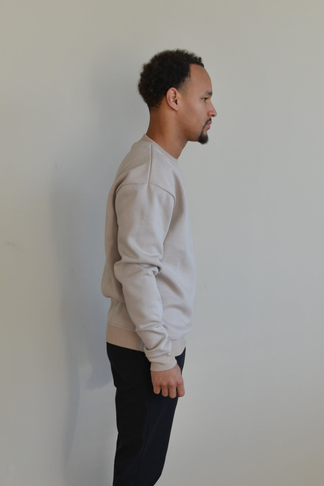 Man wearing a light gray sweatshirt against a plain white wall