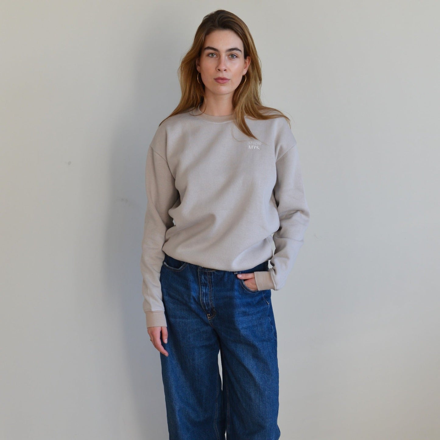 Person wearing a beige sweatshirt and blue jeans against a plain background