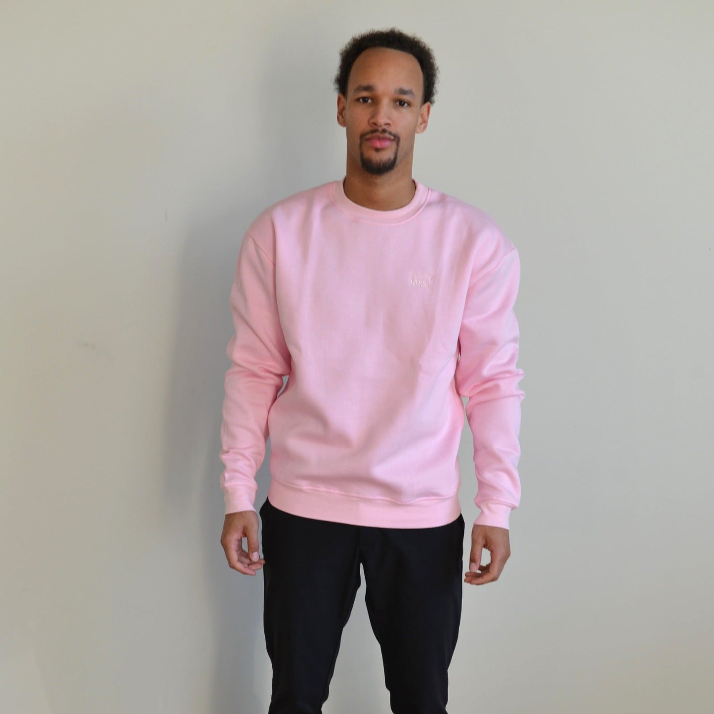 Person wearing a pink sweatshirt and black pants against a plain background