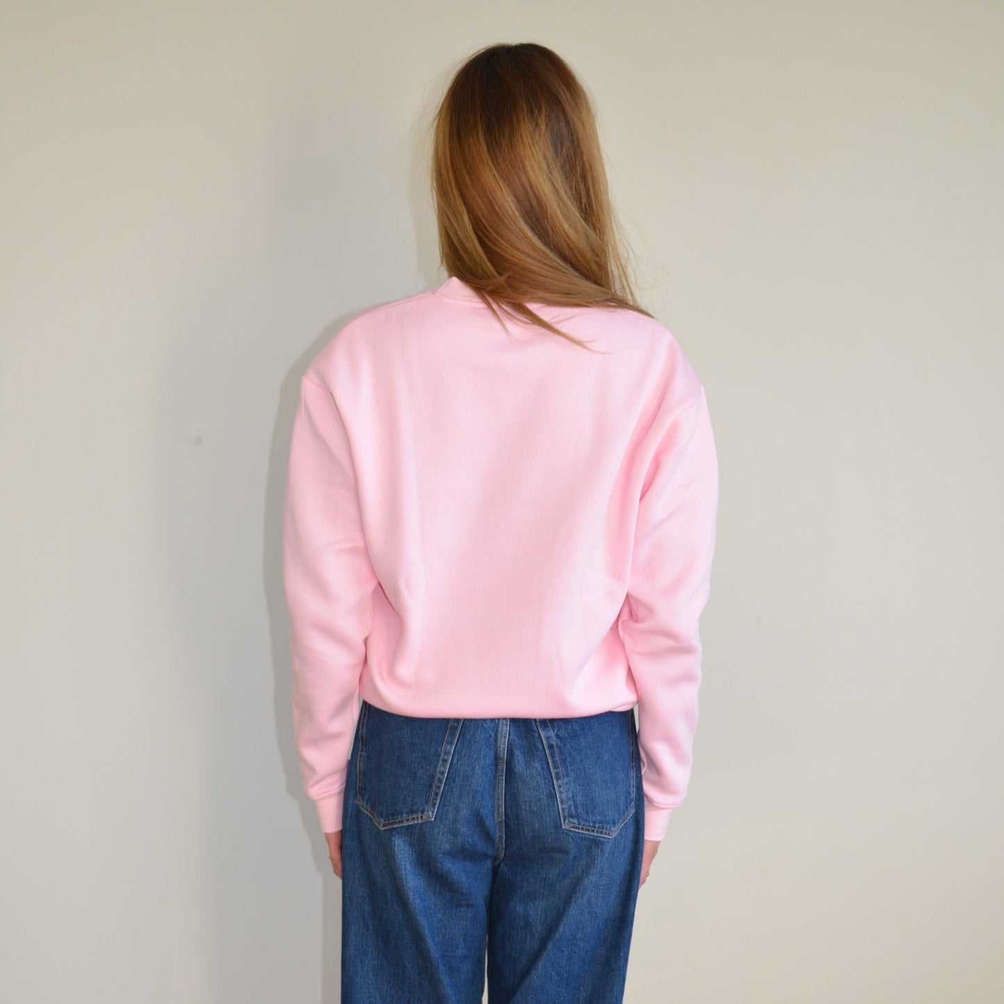 Person wearing a pink sweatshirt and blue jeans against a plain background