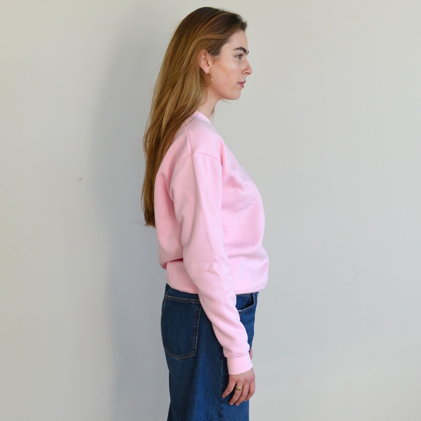 Woman wearing a pink sweatshirt and blue jeans against a plain background