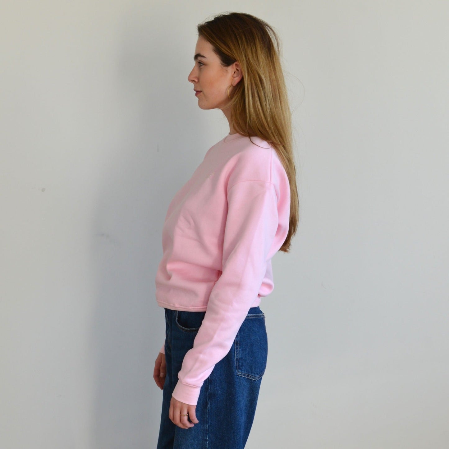 Woman wearing a pink sweatshirt and blue jeans against a plain background