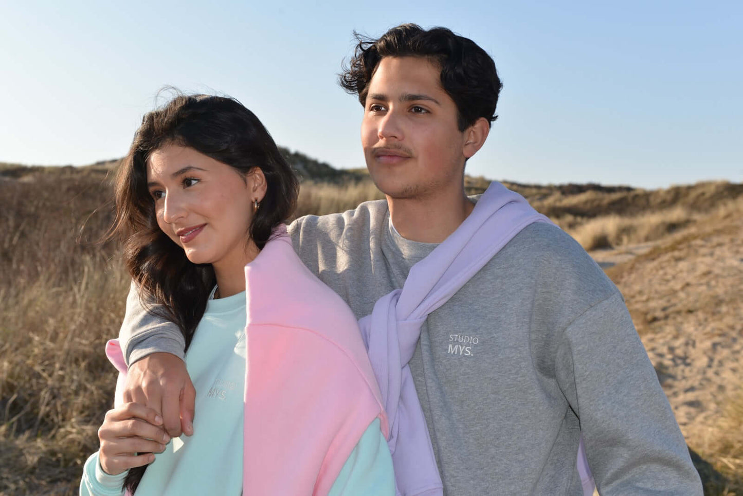 Two people standing together on a beach with a clear sky.