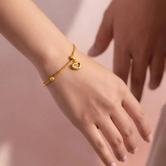 Adjustable Gold bracelet with a heart charm on a wrist against a pink background for ladies