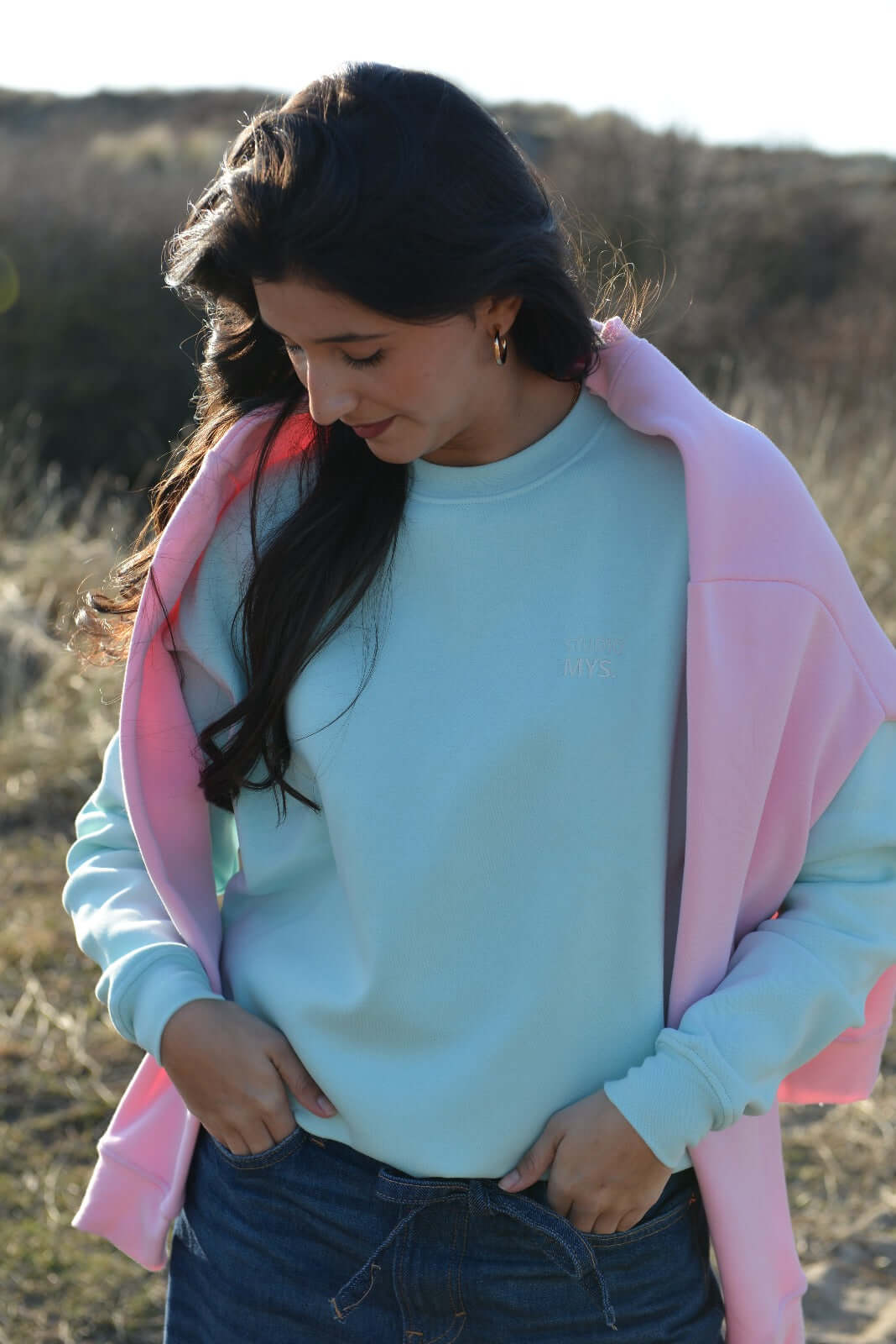 Woman wearing a light blue sweatshirt and pink jacket outdoors