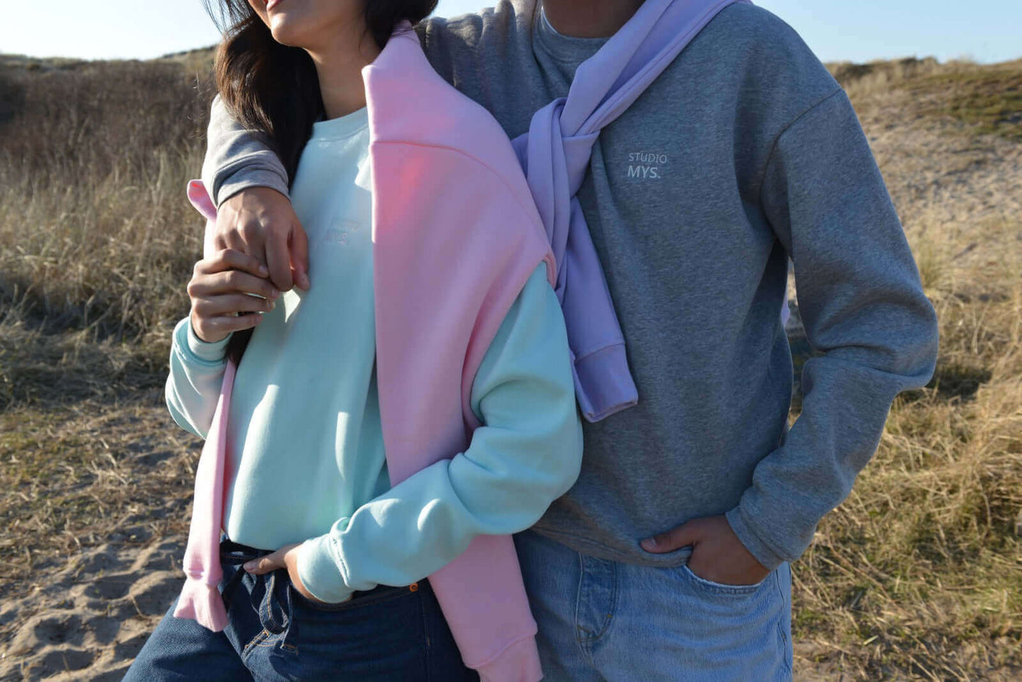 Two people standing close together in a natural setting with dry grass and clear sky.