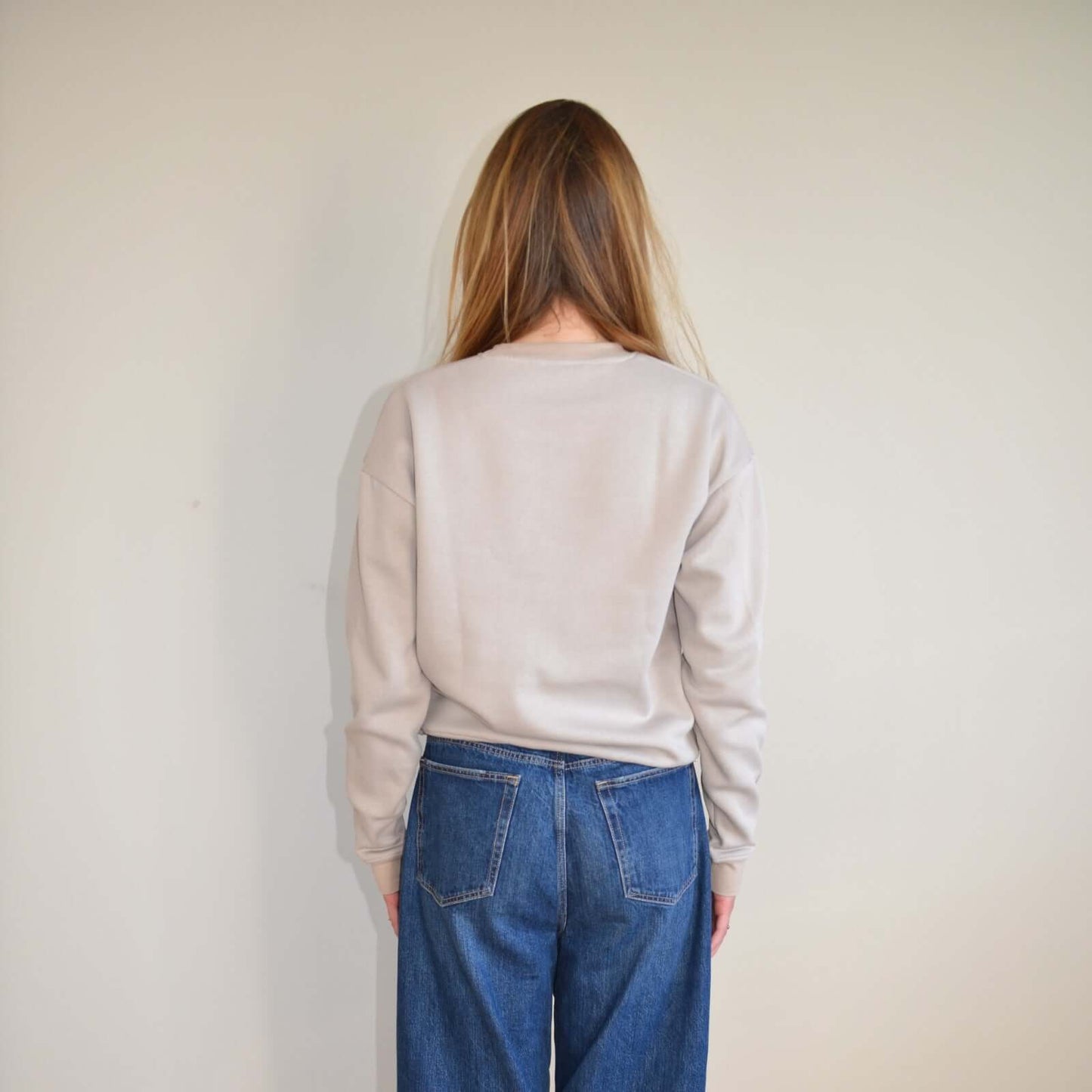 Person wearing a light gray sweater and blue jeans against a plain background