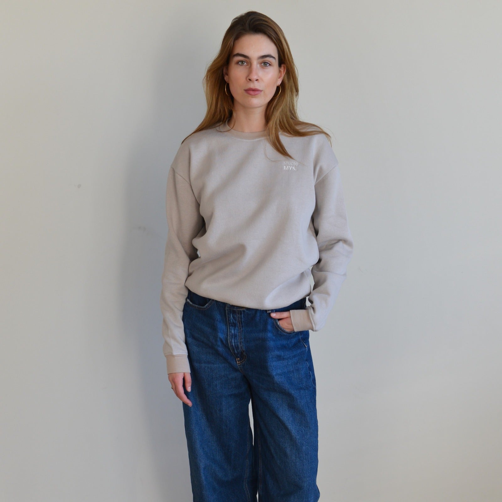 Person wearing a beige sweatshirt and blue jeans against a plain background