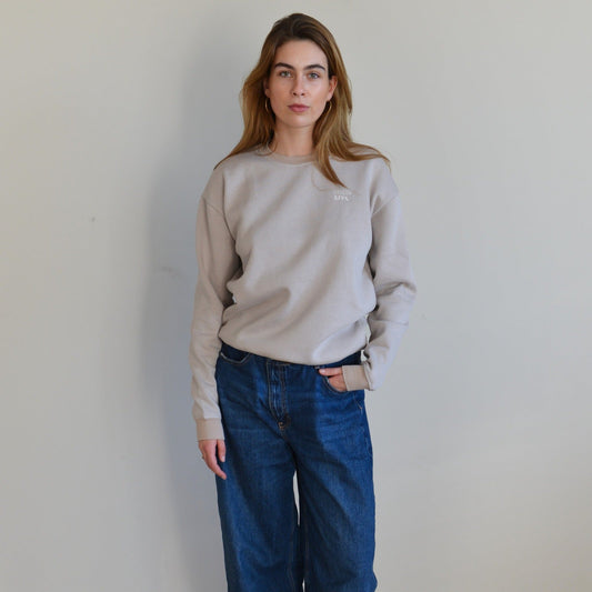 Person wearing a beige sweatshirt and blue jeans against a plain background