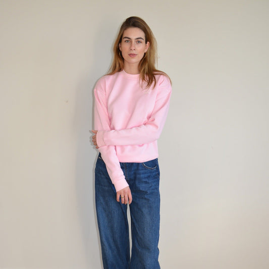 Person wearing a studio MYS pink sweater and blue jeans against a plain background