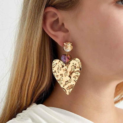 Gold heart-shaped earrings with colorful gemstones worn by a model.