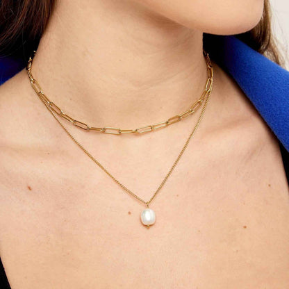 Gold chain necklace with a pearl pendant on a person wearing a blue garment.