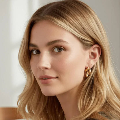Close-up of a woman with blonde hair wearing gold earrings against a neutral background
