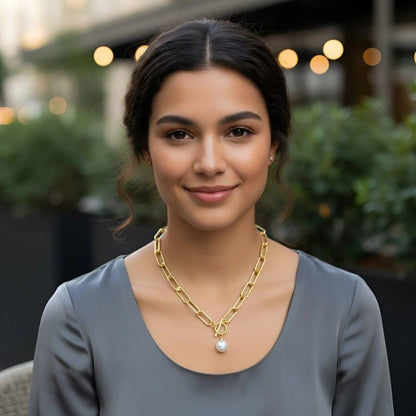 Woman wearing a gold chain necklace with a pearl pendant outdoors.