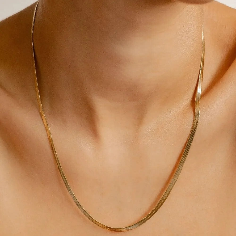 Gold necklace on a person's neck against a neutral background