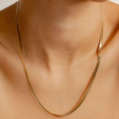 Gold necklace on a person's neck against a neutral background